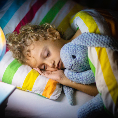 Young child sleeping peacefully in bed with a stuffed bunny